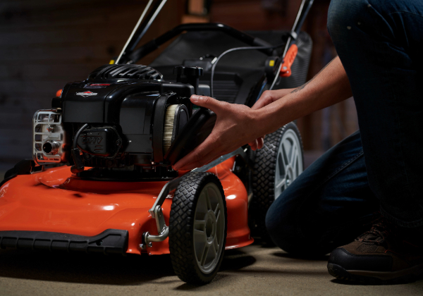 A person changing an air filter on a Briggs & Stratton push mower engine. 